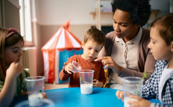 Black female teacher teaching group of kids to plant seeds at preschool.