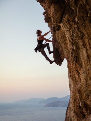 Young woman climbing challenging route at sunset